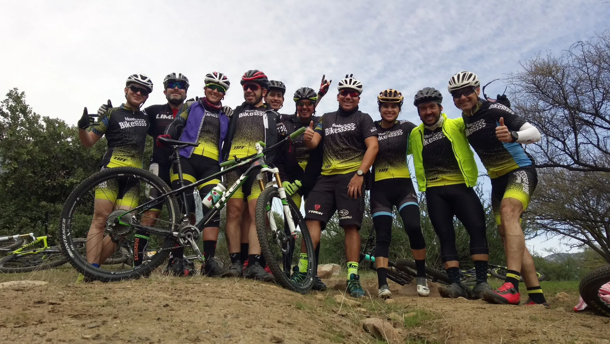 Diez ciclistas, casi todos con el jersey negro y amarillo de Mundobikes posando en un cerro junto a una MTB, con otras bicis en el suelo