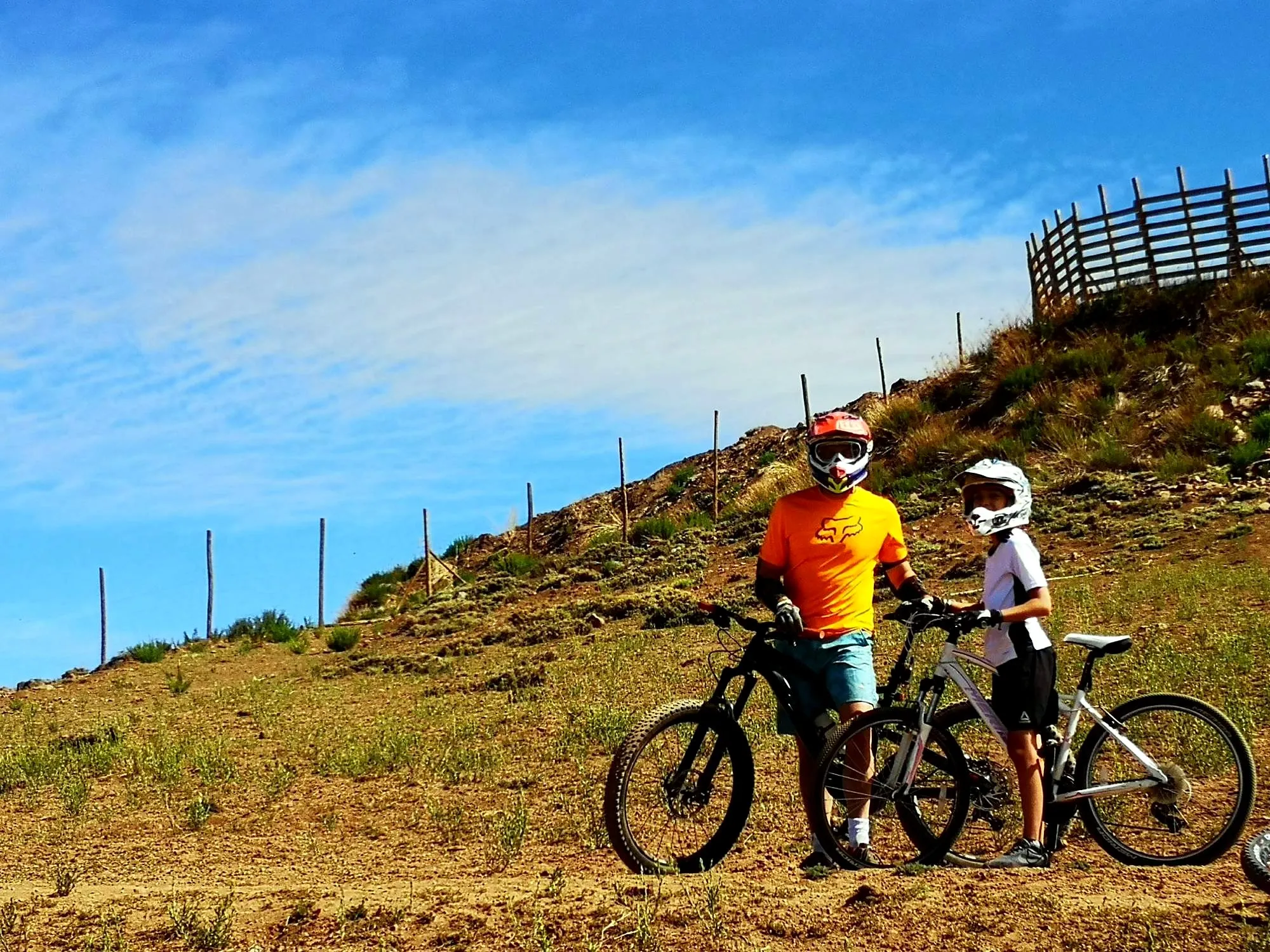 Padre e hijo con casco integral y sus bicis de montaña en la ladera de un bike park
