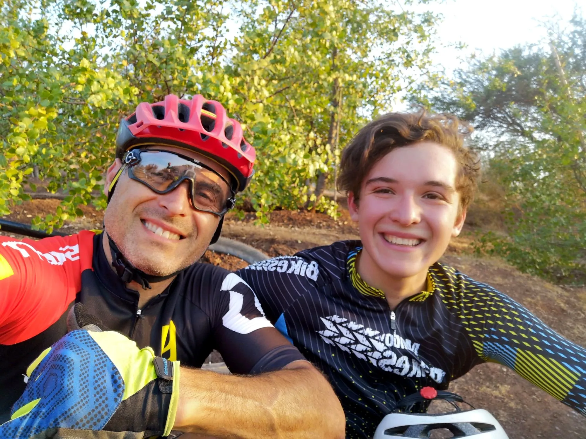Padre e hijo adolescente sonriendo en una selfie después de una salida en bici por un sendero
