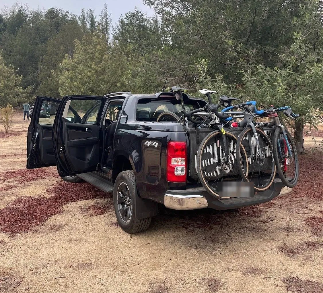 Camioneta con la puerta abierta en un claro entre árboles, con tres bicis de gravel colgadas del pad Evoc en el portalón