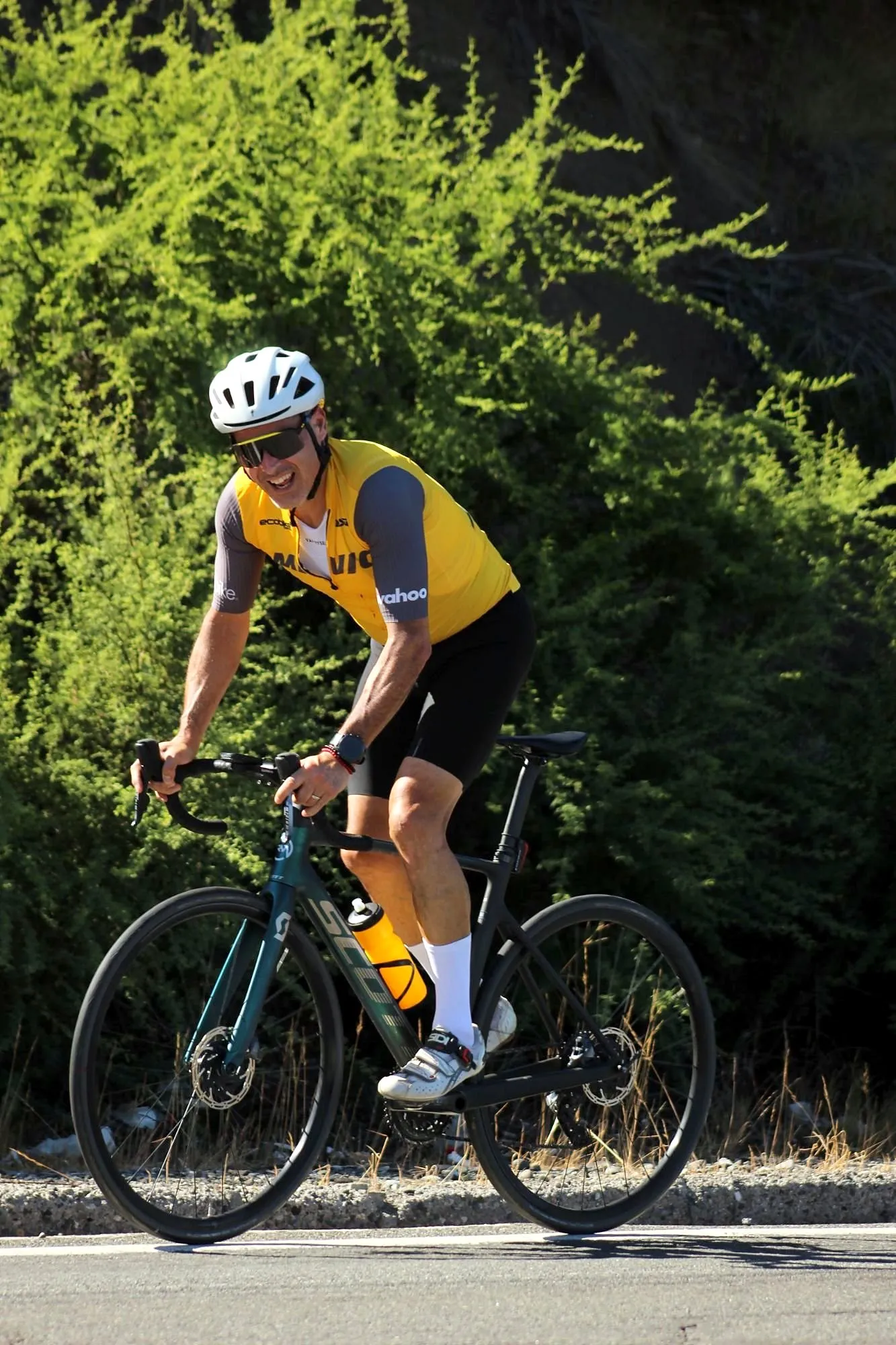 Ciclista en bici de ruta subiendo por una carretera pavimentada, con vegetación al costado