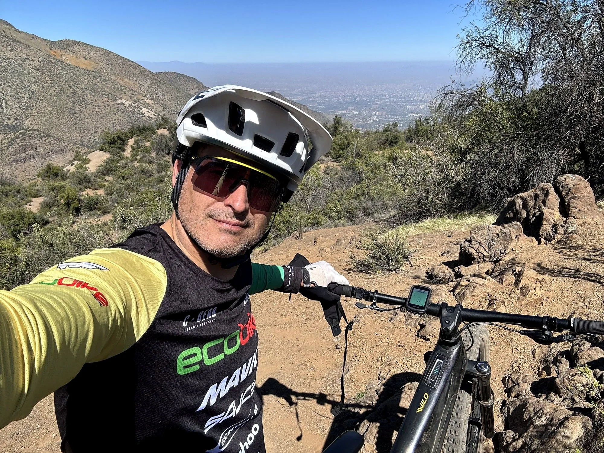 Ciclista en un sendero de tierra de la precordillera con su eMTB y el ciclocomputador en el manubrio, con la ciudad abajo